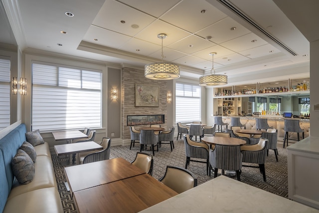 carpeted dining area featuring a tray ceiling, a community bar, crown molding, and a tiled fireplace