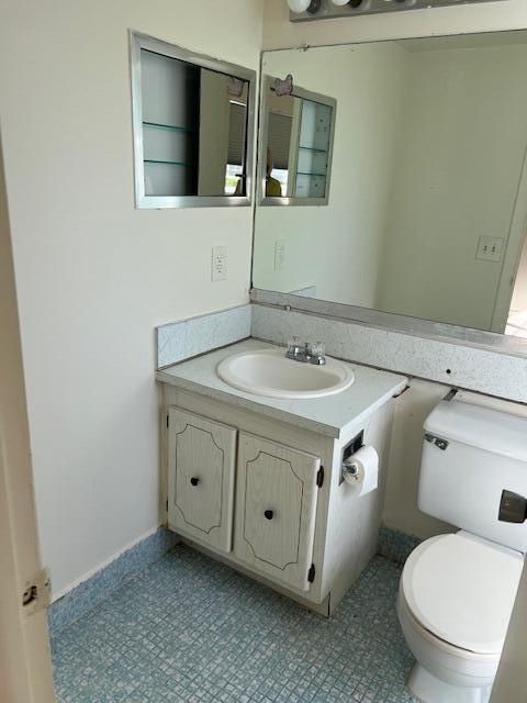 half bath featuring tile patterned floors, toilet, and vanity