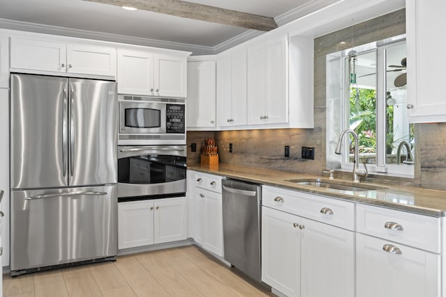 kitchen with stainless steel appliances, white cabinetry, a sink, and backsplash