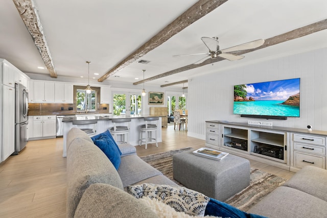 living area featuring light wood-style floors, beamed ceiling, ceiling fan, and visible vents