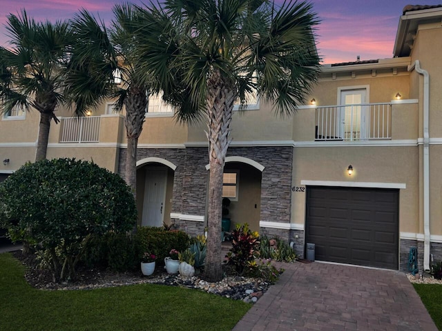 multi unit property featuring stone siding, stucco siding, decorative driveway, and an attached garage