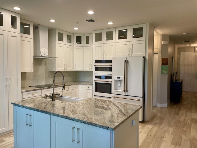 kitchen with white appliances, visible vents, light wood-style flooring, a sink, and wall chimney exhaust hood