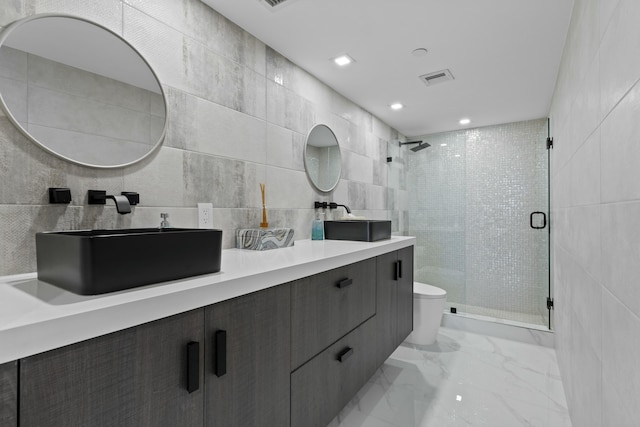 full bath featuring toilet, marble finish floor, a stall shower, a sink, and tile walls