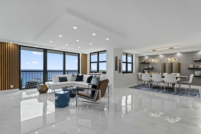 living area with recessed lighting, a water view, marble finish floor, and a wall of windows