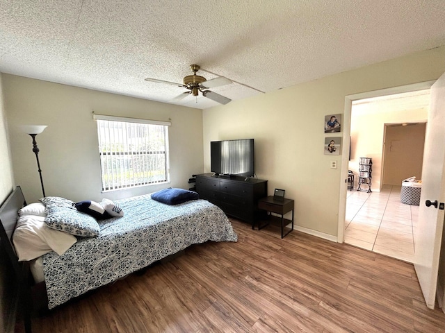 bedroom featuring ceiling fan, baseboards, a textured ceiling, and wood finished floors