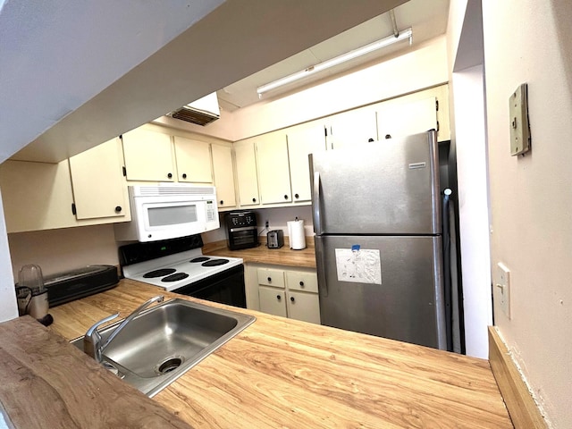 kitchen featuring white microwave, freestanding refrigerator, a sink, range with electric cooktop, and light countertops