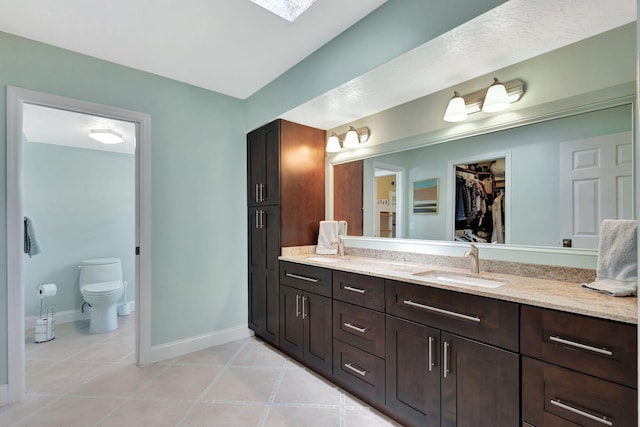 full bathroom with tile patterned floors, toilet, vanity, baseboards, and a spacious closet