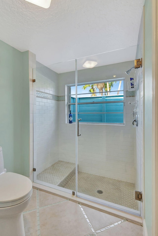 bathroom featuring tile patterned floors, toilet, a stall shower, and a textured ceiling