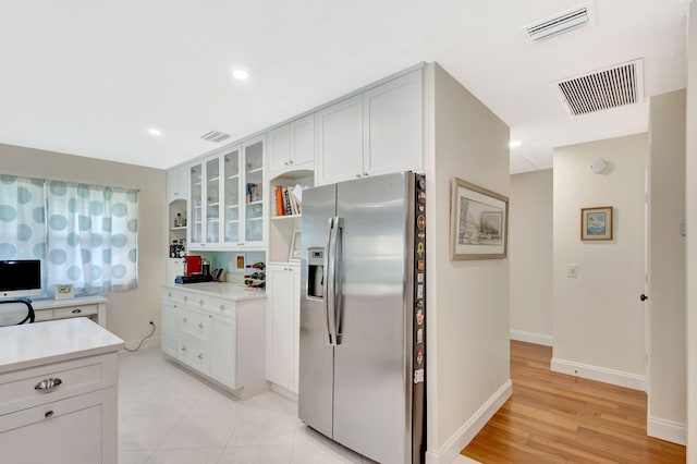 kitchen featuring open shelves, visible vents, stainless steel fridge with ice dispenser, and light countertops