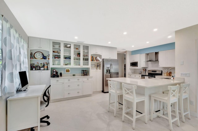 kitchen featuring a breakfast bar, a peninsula, a sink, stainless steel appliances, and wall chimney range hood