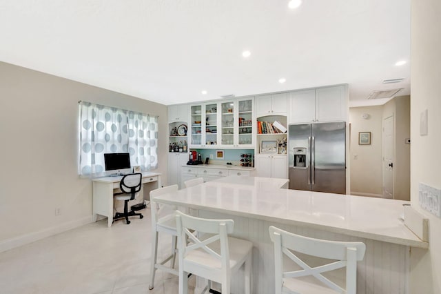 kitchen with recessed lighting, a peninsula, a breakfast bar area, stainless steel fridge with ice dispenser, and glass insert cabinets