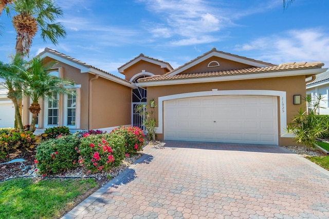 view of front facade with stucco siding, an attached garage, a tile roof, and decorative driveway