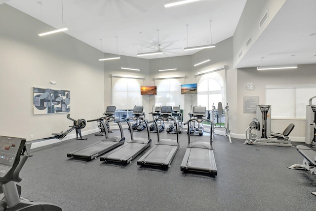 gym with visible vents, baseboards, a towering ceiling, and a ceiling fan