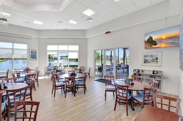 dining room with baseboards, visible vents, light wood finished floors, a high ceiling, and a water view