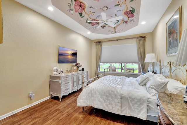 bedroom featuring a tray ceiling, recessed lighting, wood finished floors, and baseboards