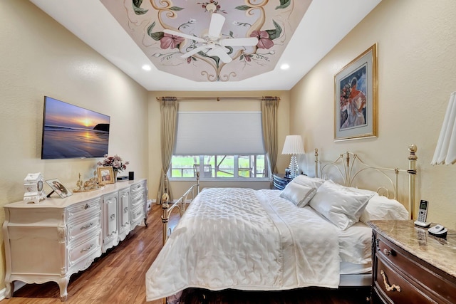 bedroom featuring recessed lighting, a tray ceiling, and wood finished floors