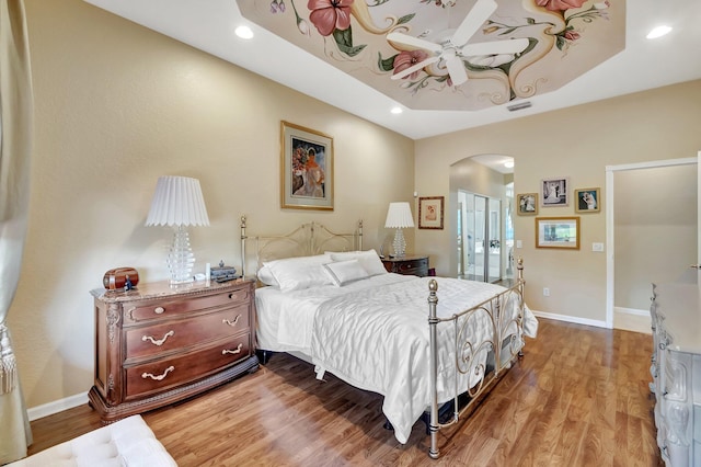 bedroom featuring a raised ceiling, wood finished floors, arched walkways, and baseboards