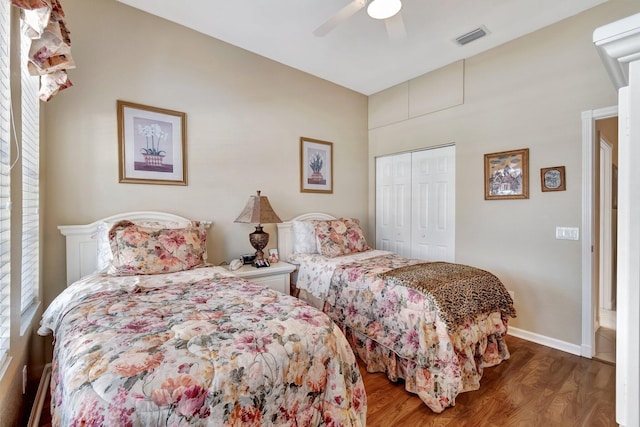 bedroom with a ceiling fan, visible vents, wood finished floors, baseboards, and a closet