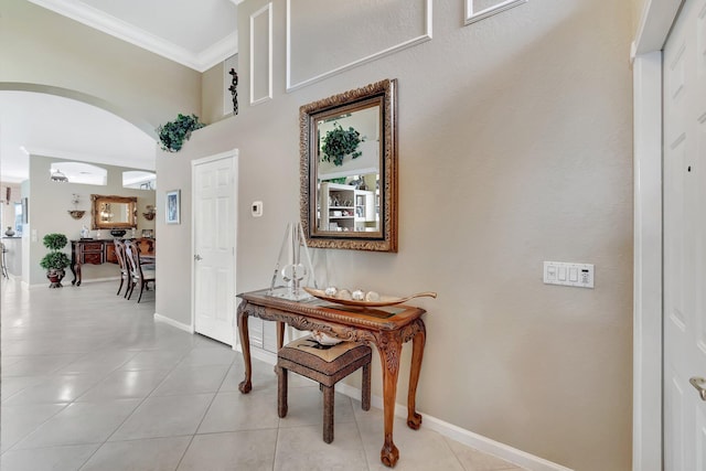 hall featuring light tile patterned floors, baseboards, arched walkways, and ornamental molding