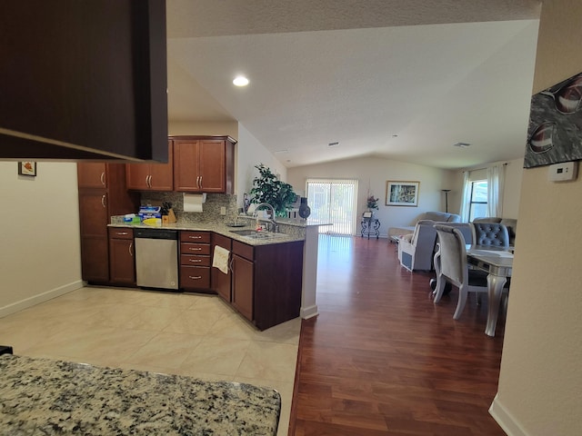 kitchen with open floor plan, lofted ceiling, a peninsula, stainless steel dishwasher, and a sink