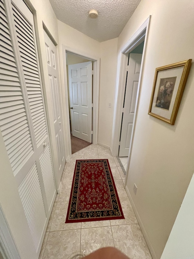 hallway with light tile patterned floors, a textured ceiling, and baseboards