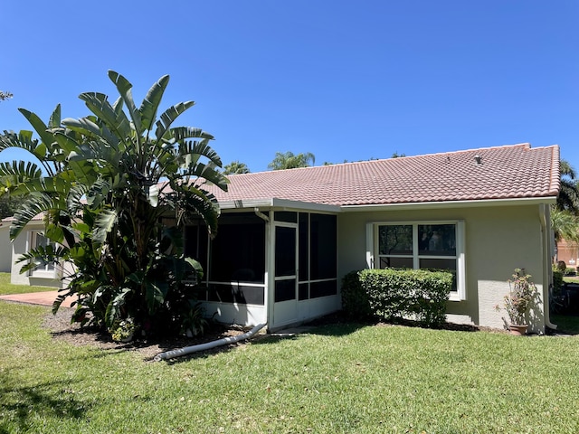 rear view of house with a tiled roof, a lawn, a sunroom, and stucco siding