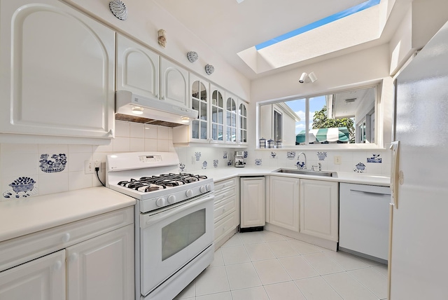 kitchen with glass insert cabinets, under cabinet range hood, a skylight, white appliances, and a sink