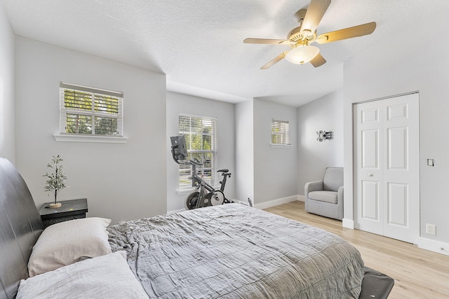 bedroom featuring light wood finished floors, ceiling fan, baseboards, vaulted ceiling, and a textured ceiling