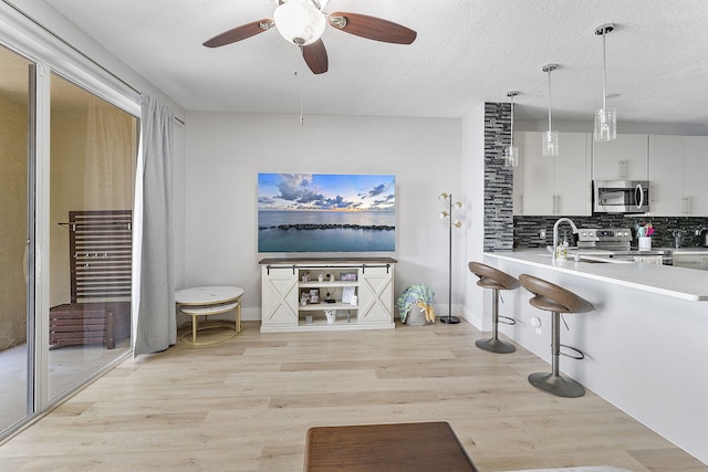 kitchen with light wood-type flooring, backsplash, appliances with stainless steel finishes, light countertops, and ceiling fan