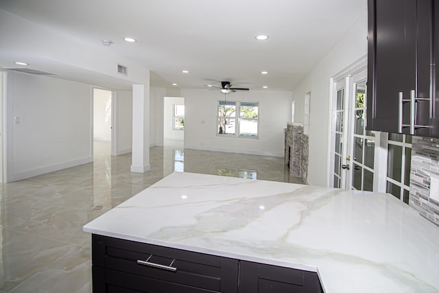 kitchen with marble finish floor, ceiling fan, open floor plan, light stone countertops, and dark cabinets