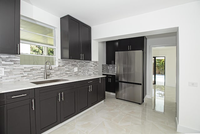 kitchen featuring backsplash, a healthy amount of sunlight, light countertops, freestanding refrigerator, and a sink