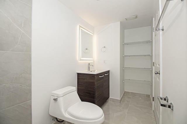 bathroom with visible vents, a walk in closet, toilet, marble finish floor, and vanity