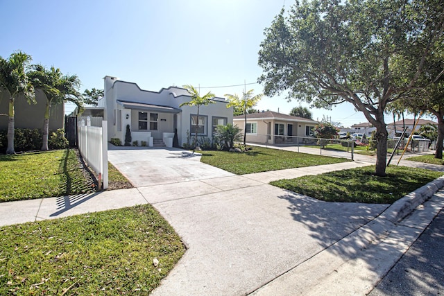 view of front of home with stucco siding, concrete driveway, a front yard, and fence