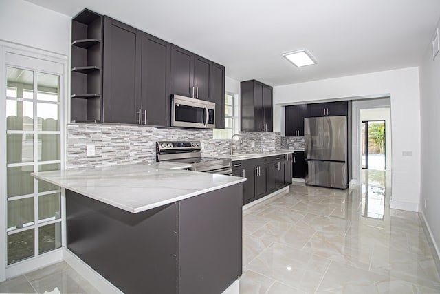 kitchen with tasteful backsplash, open shelves, appliances with stainless steel finishes, a peninsula, and a sink