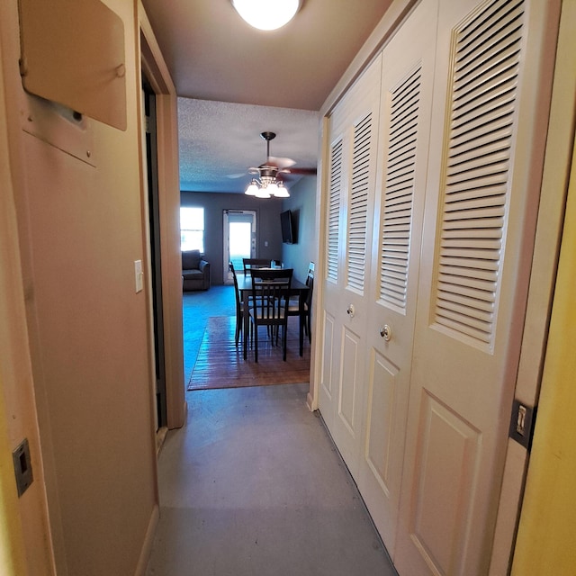 hall with baseboards, a textured ceiling, and concrete floors