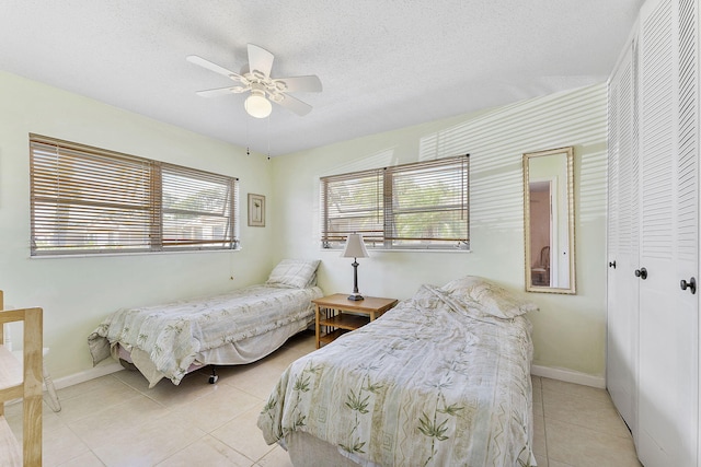 bedroom with ceiling fan, light tile patterned flooring, baseboards, and a textured ceiling