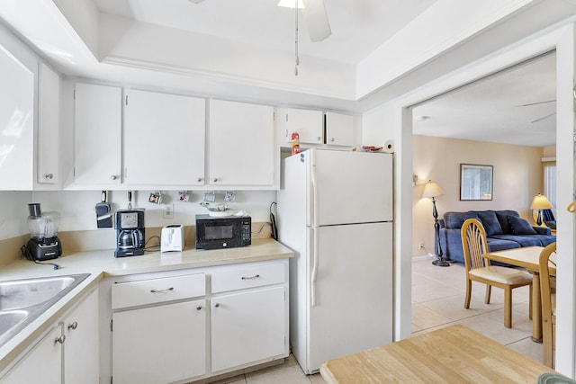 kitchen with black microwave, light tile patterned floors, freestanding refrigerator, white cabinetry, and a ceiling fan