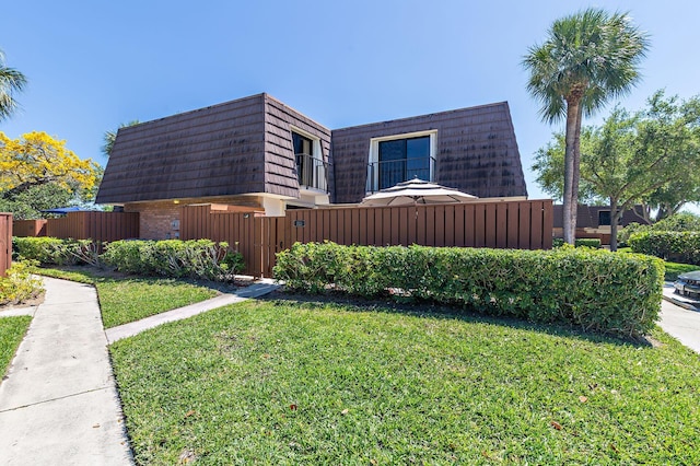 view of side of property with mansard roof, a lawn, and fence