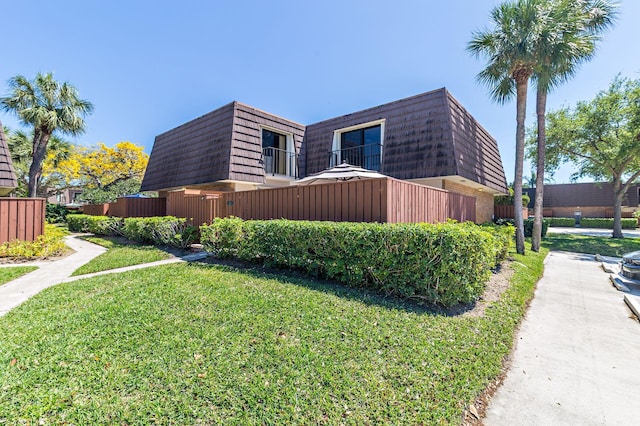 view of side of property featuring a lawn, mansard roof, and fence