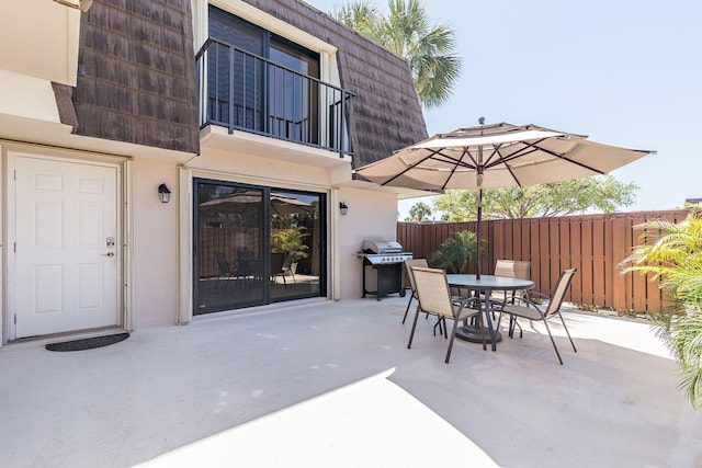 view of patio with a balcony, outdoor dining space, and fence