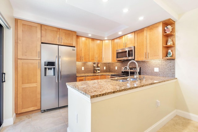 kitchen featuring a sink, backsplash, appliances with stainless steel finishes, a peninsula, and light stone countertops