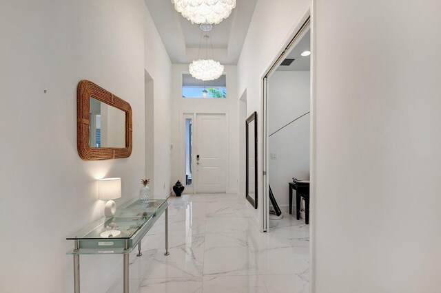 7855 Wildflower Shores Dr, Delray Beach, FL 33446 - hallway with visible vents, an inviting chandelier, a towering ceiling, marble finish floor, and a raised ceiling