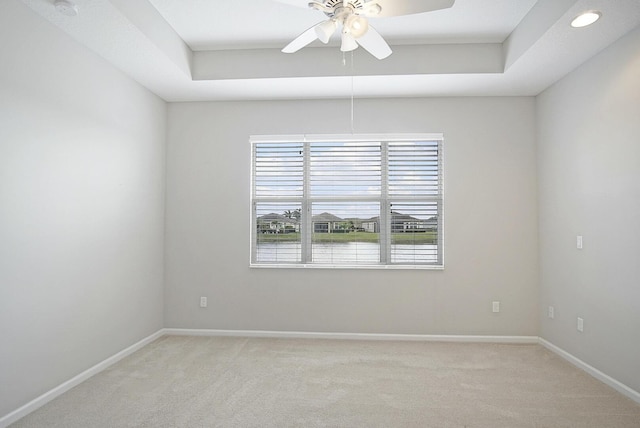 empty room with a raised ceiling, a ceiling fan, and light carpet