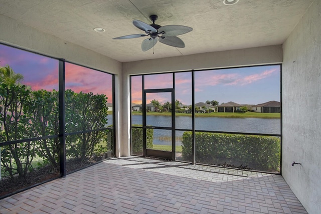 unfurnished sunroom featuring a ceiling fan and a water view