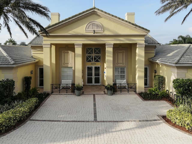 view of exterior entry featuring covered porch, stucco siding, a chimney, french doors, and a tile roof