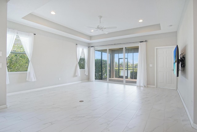 unfurnished room with marble finish floor, baseboards, a tray ceiling, and ceiling fan