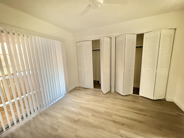 unfurnished bedroom featuring a ceiling fan, two closets, and light wood-style floors