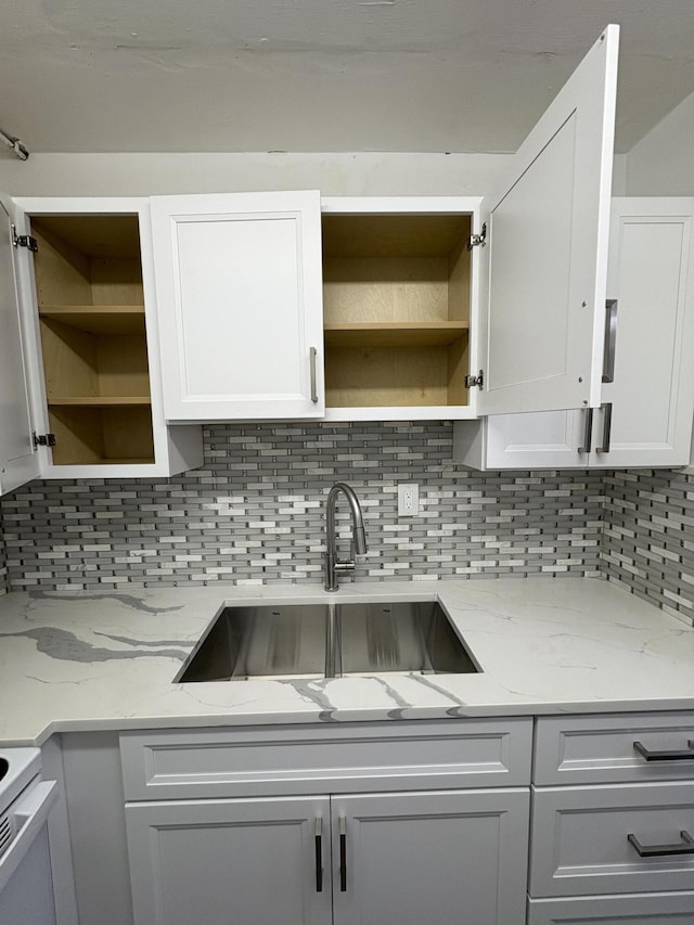 kitchen with tasteful backsplash, open shelves, a sink, light stone counters, and white cabinets