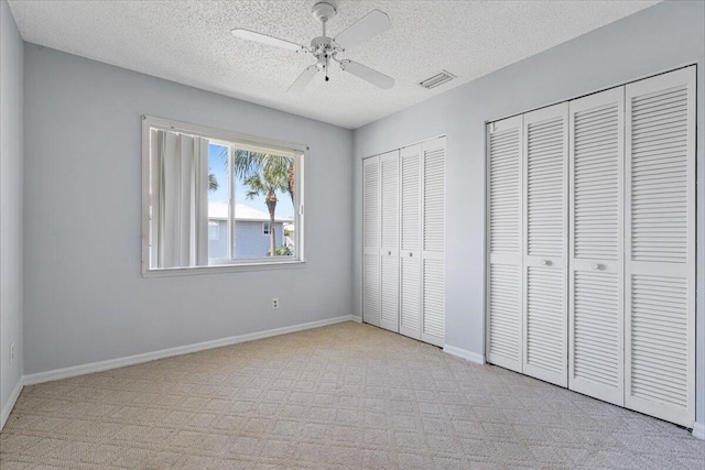 unfurnished bedroom with visible vents, carpet floors, baseboards, multiple closets, and a textured ceiling