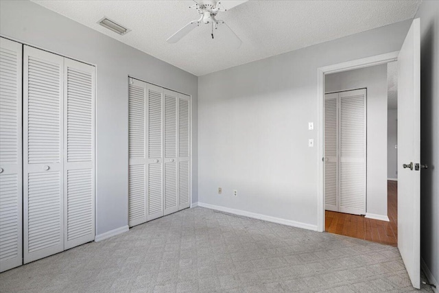 unfurnished bedroom with baseboards, visible vents, carpet floors, a textured ceiling, and two closets